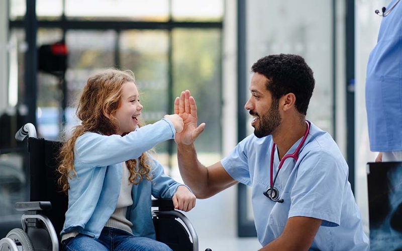 Young multiracial doctor having fun with little girl on wheelchair.