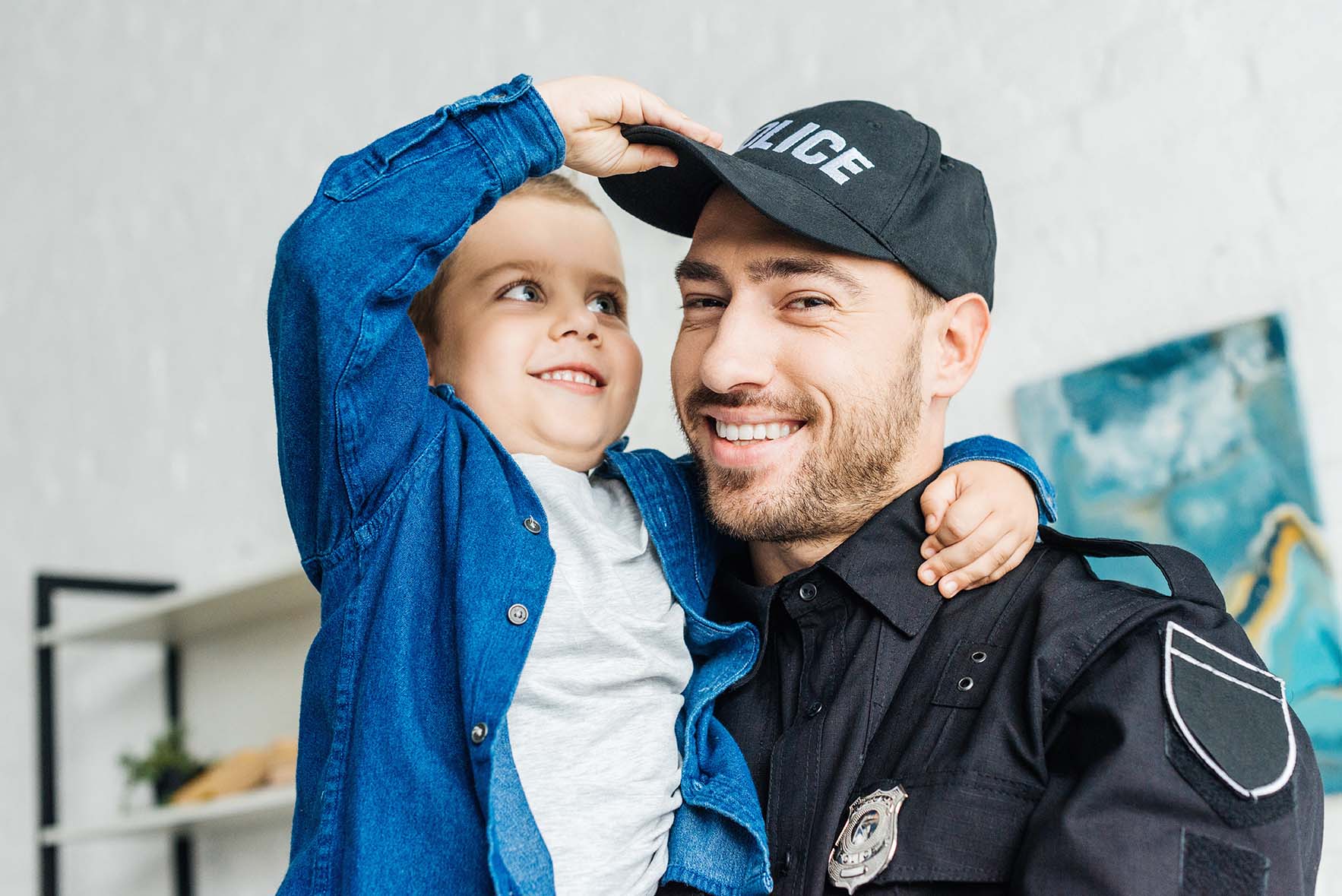 close-up portrait of smiling young father in police uniform carrying his little son and looking at camera